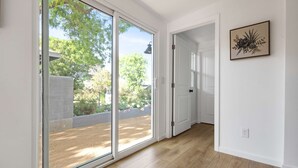 Ein Zimmer mit einer Schiebetür zum Garten, einer weißen Tür und einem gerahmten Kunstwerk an der Wand.