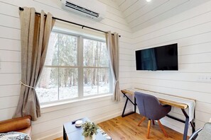 Een kamer met een houten vloer, een bureau met stoel, een bed, een televisie aan de muur en een raam met gordijnen.