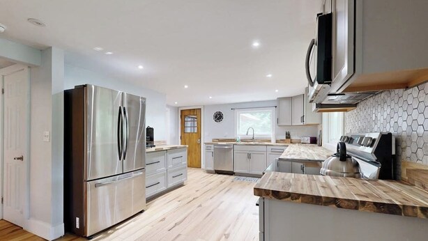 Una cocina moderna con electrodomésticos de acero inoxidable, encimeras de madera y un salpicadero de azulejos.