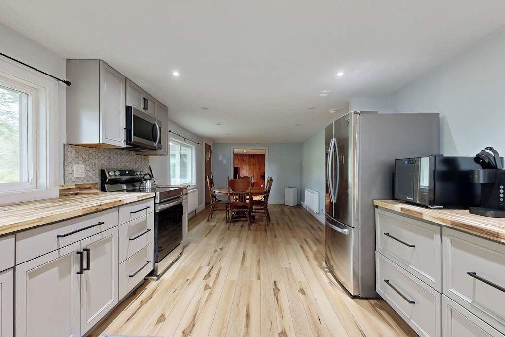 A modern kitchen with white cabinets, a wooden countertop, a stainless steel refrigerator, and a microwave.
