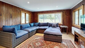 Una habitación con un sofá seccional grande, una mesita, un televisor y ventanas amplias.