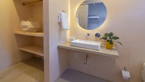 A bathroom with a white sink, a round mirror, a towel rack, a shelf with a white bag, and a potted plant. - Apt. Suite with pool in colonial house  Downtown (Santa Marta)