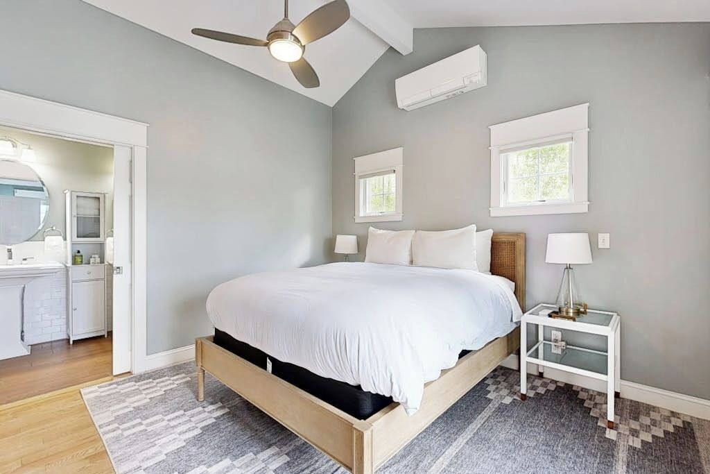 Un dormitorio con una cama, un ventilador de techo, una mesita de noche y una ventana.