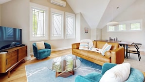 Een woonkamer met een bank, fauteuil, televisie, en een eethoek met tafel en stoelen.