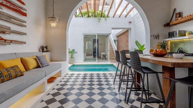 Een moderne keuken met een geruite vloer, een eethoek met barstoelen en een zwembad zichtbaar door een boog.