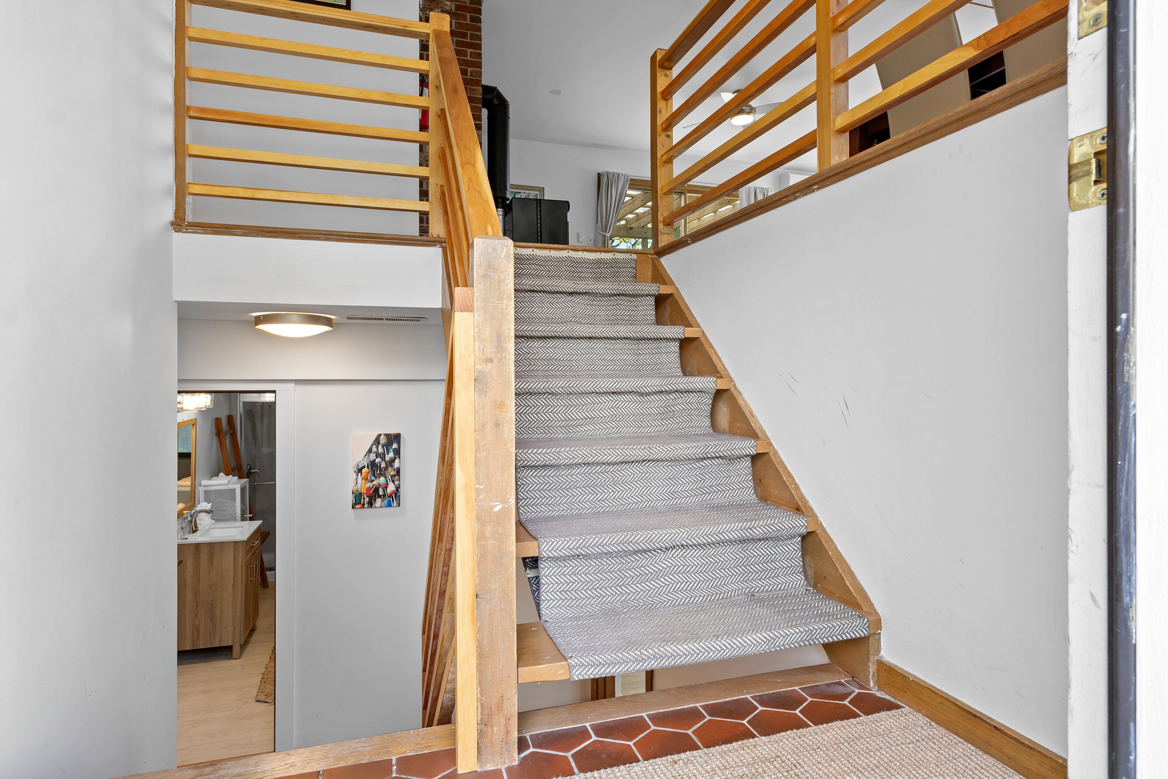 Un escalier en bois, recouvert d’une moquette à motifs en chevrons, mène à un palier situé au deuxième étage.