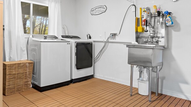 A laundry room with a washing machine, dryer, and a sink with cleaning supplies. - Evelyn's River Front Retreat- Spacious House with Modern Comforts and Nature (Cushing)