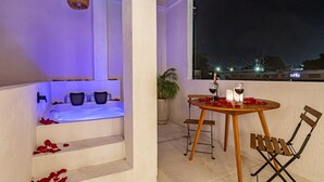 A balcony with a table set for two, a chair, a potted plant, and a view of the city at night. - spectacular apartasuit in hotelb outique (Santa Marta)