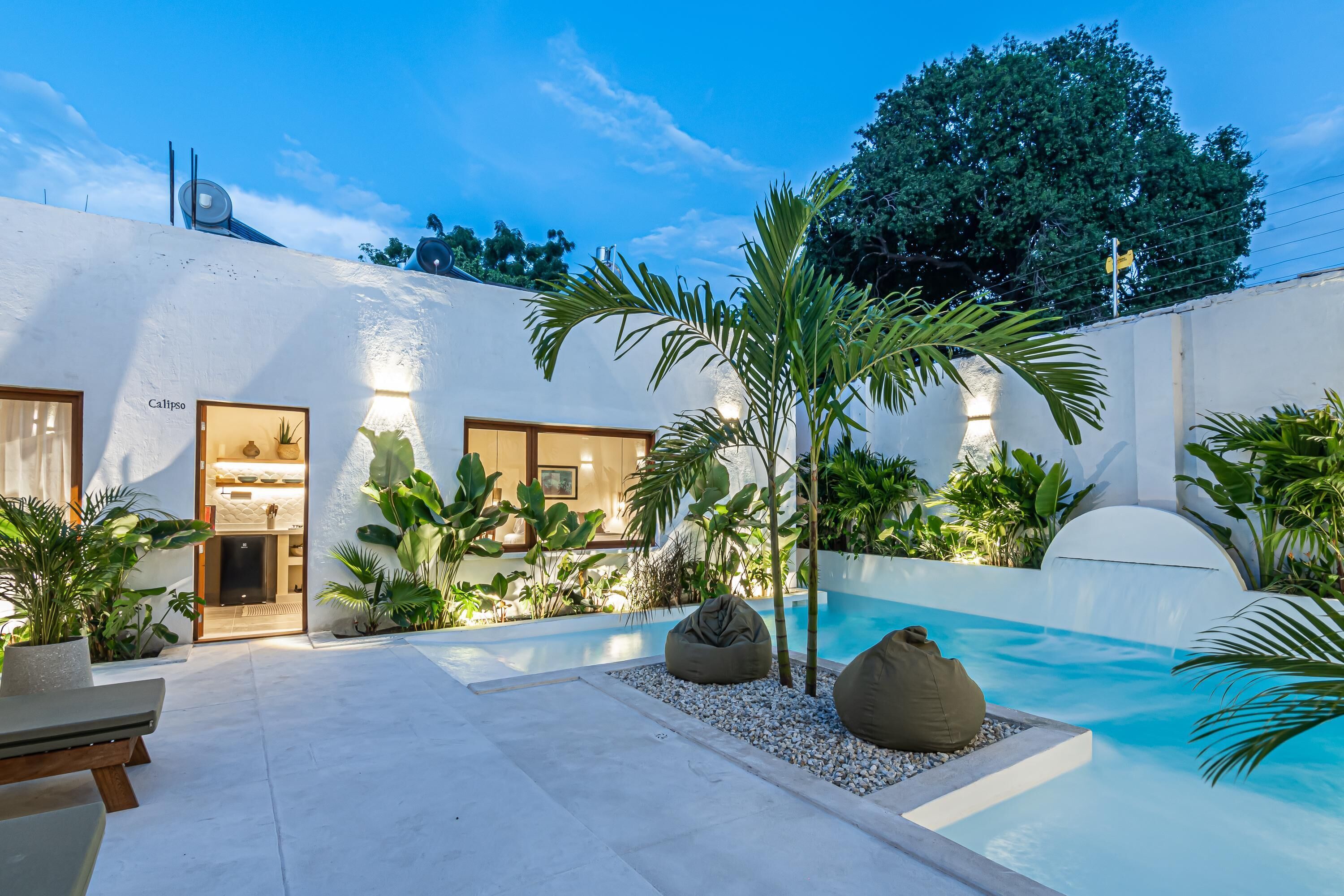 A modern outdoor pool area with a white exterior, a small waterfall, and various plants.
