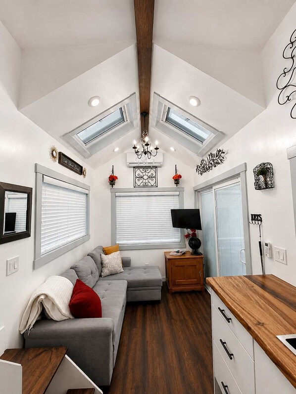 Un interior moderno con techo estilo loft, un sofá gris, una mesa de madera y un televisor sobre un mueble de madera.