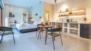 Een moderne hotelkamer met een bed, een eettafel met stoelen, een keukenhoek met planken en een kleine koelkast.