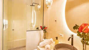 Een moderne badkamer met een glazen douchecabine, een rond wastafeltje en een vaas met een rode bloem.