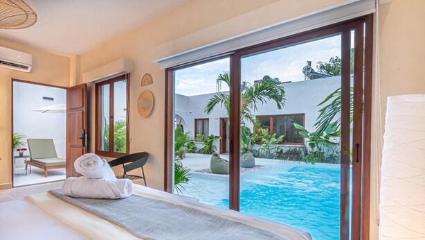 Een hotelkamer met een bed, uitzicht op een zwembad en een deur naar een balkon.
