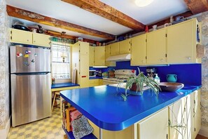 Eine Küche mit gelben Schränken, einer blauen Arbeitsplatte, einem Edelstahlkühlschrank und einer Holzbalkendecke.