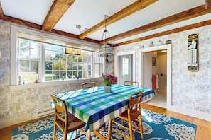 A dining area with a table set for four, wooden chairs, a patterned rug, and a window with a view of greenery.