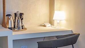 Una kitchenette con cafetera, hervidor, una botella, teléfono y lámpara sobre una encimera.