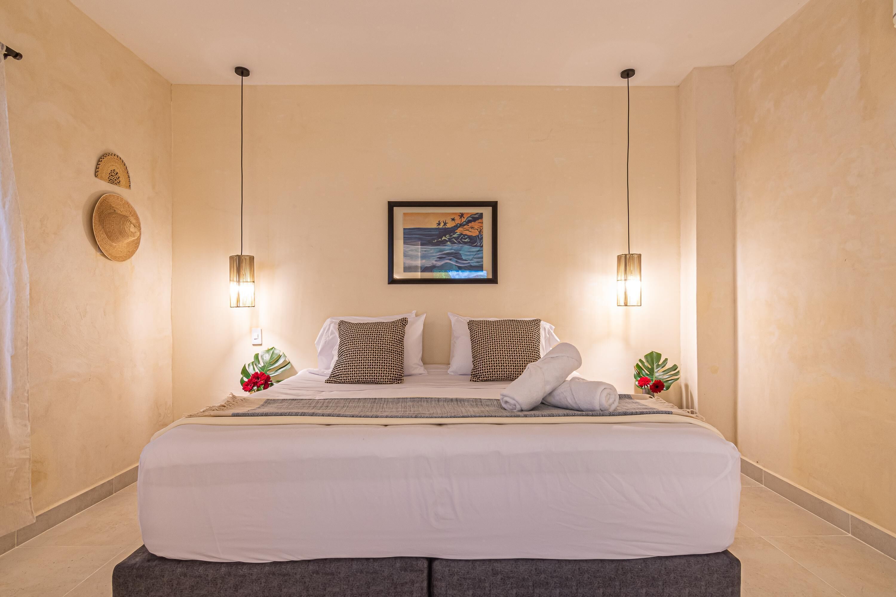 A neatly made bed with pillows, a framed picture on the wall, and two wall-mounted lamps.