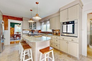 A kitchen with a central island, bar stools, a refrigerator, and a stove.