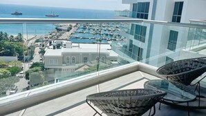 Ein Balkon mit Korbmöbeln, Blick auf einen Yachthafen mit Booten und ein modernes Gebäude mit großen Fenstern.