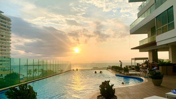 Ein Pool auf dem Dach mit freiem Blick auf Sonnenuntergang und Meer, umgeben von Liegestühlen und Topfpflanzen.