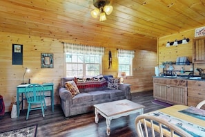 Interior d'una cabana acollidora amb sostre de fusta, un sofà, una taula de dinar, una zona de cuina i un escriptori.
