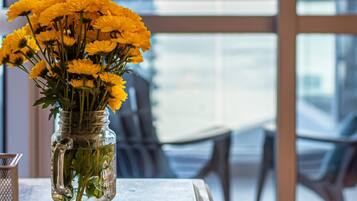 A clear view of a cityscape through large windows, a vase with yellow flowers on a table, and a metal candle holder.