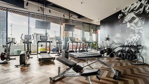 Une salle de sport moderne équipée de machines de cardio, de postes d’entraînement avec poids et ornée d’une fresque murale.