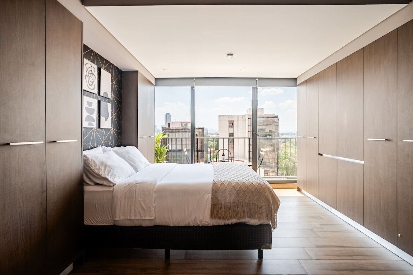 A modern bedroom with a large bed, wardrobe, and a balcony with a city view.