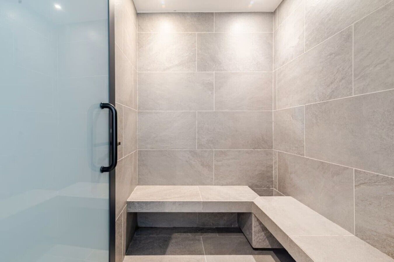 A modern shower with a glass door, tiled walls, and a bench.