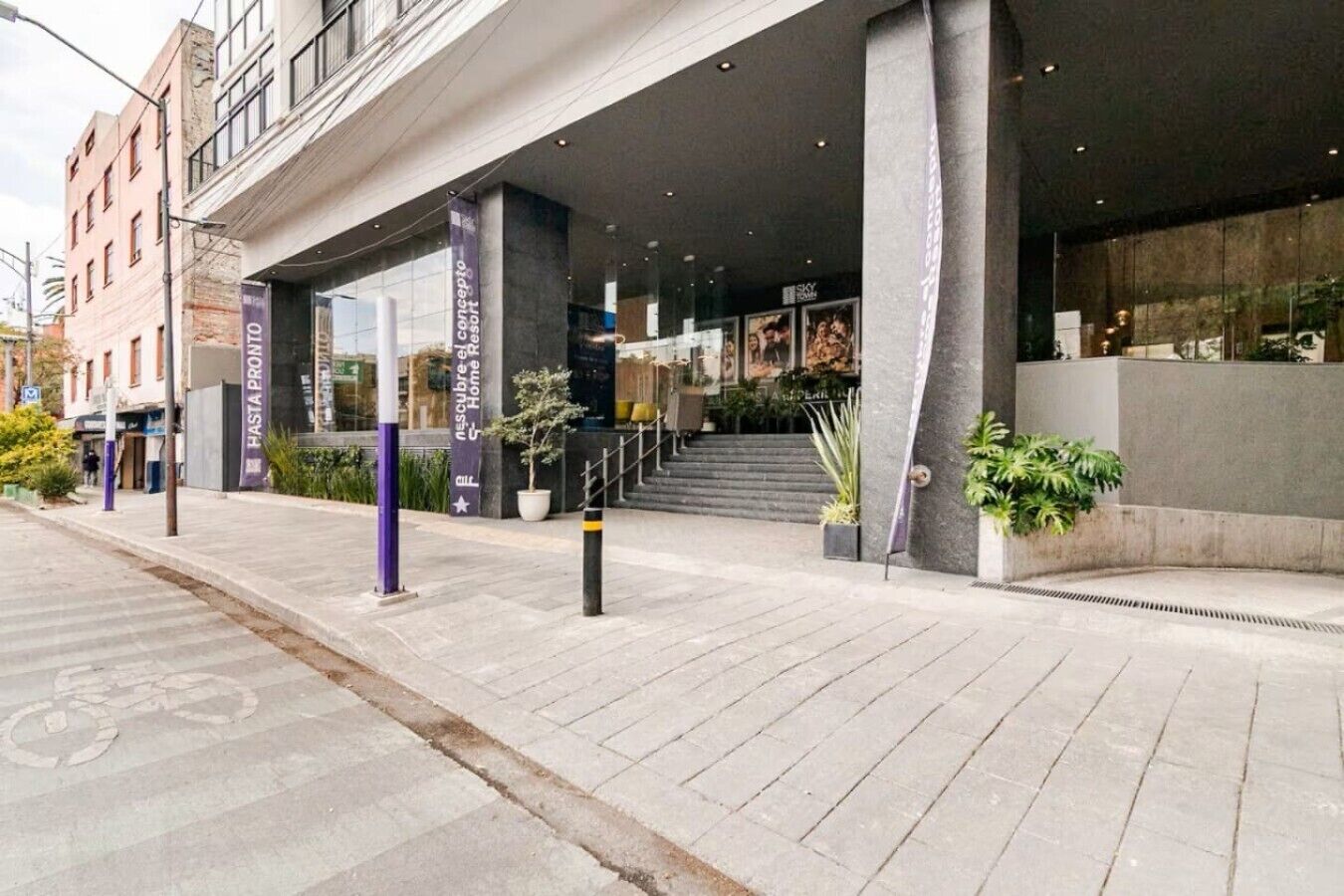 A modern hotel entrance with a covered outdoor area, a staircase leading to the entrance, and potted plants.