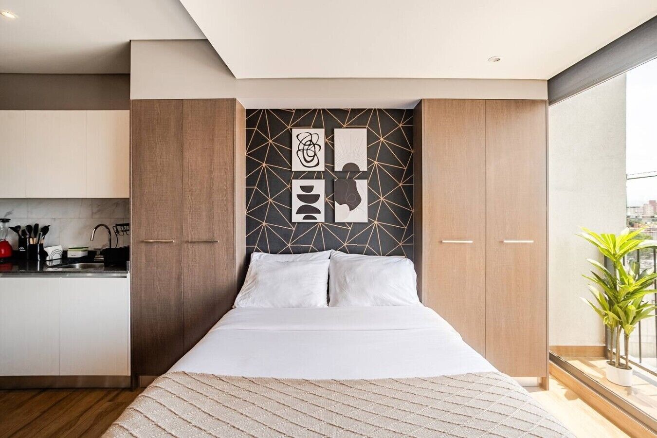 Une chambre avec un lit, un coin cuisine et un mur orné d’un motif géométrique.