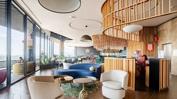 Un espace lounge moderne, doté de sièges confortables, d’un bar et offrant une vue dégagée grâce à de grandes fenêtres.