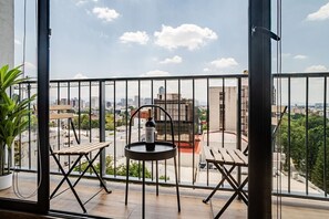 Ein Balkon mit Blick auf eine Stadtlandschaft, eine Weinflasche und zwei Holzstühle.