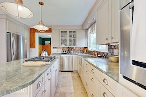 A modern kitchen with stainless steel appliances, a granite countertop, and white cabinetry. - Coastal Serenity Retreat with Ocean Views, Spacious Porch and Modern Comforts (Sullivan)