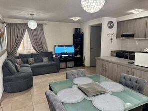 Una sala de estar con sofá, televisor y una mesa de comedor con individuales.
