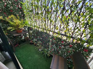 Un balcón con césped artificial, plantas en macetas y una silla de mimbre.