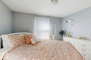 Un dormitorio con cama, mesita de noche, espejo y ventilador de pared.