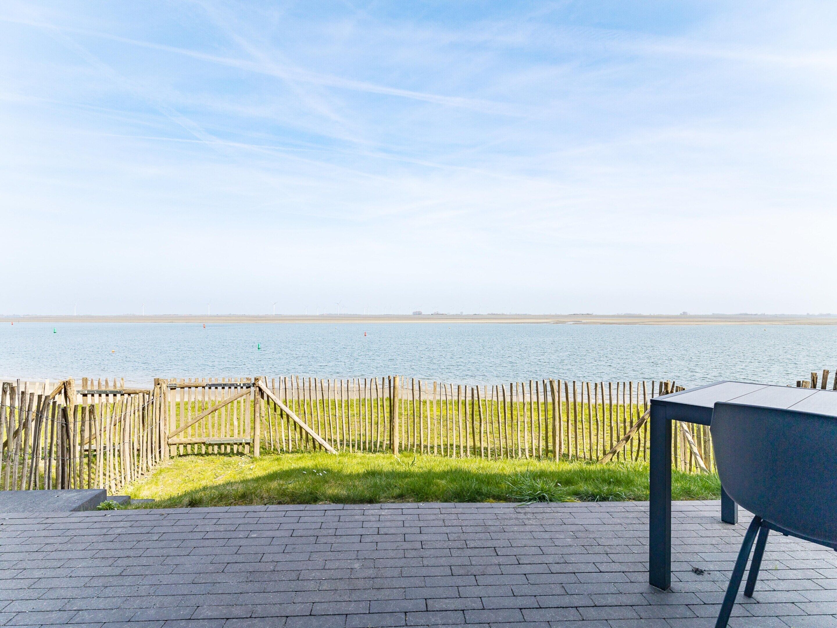 Une terrasse avec vue sur un plan d’eau, une clôture en bois et un barbecue.