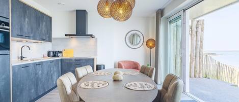 A modern kitchen with dark cabinets, a round dining table with chairs, and a view of the sea through large windows.