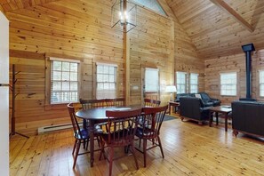 A log cabin interior with a dining table, chairs, a sofa, and a fireplace. - Inviting dog-friendly cabin with wooded views, full kitchen & firepit (Northport)
