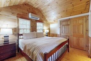 A wooden cabin bedroom with a bed, two bedside lamps, a dresser, and a door. - Inviting dog-friendly cabin with wooded views, full kitchen & firepit (Northport)