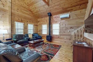 A log cabin interior with a fireplace, leather sofas, a coffee table, and a patterned rug. - Inviting dog-friendly cabin with wooded views, full kitchen & firepit (Northport)