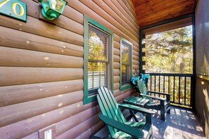 Een houten chalet met een veranda, twee ramen met luiken en twee Adirondack stoelen.