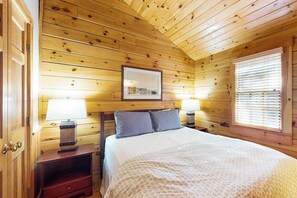 Habitación con paneles de madera, una cama, dos lámparas de noche, un cuadro en la pared y una ventana con persianas.