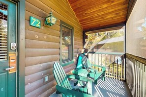 En stuga av trä med en veranda, nummer 72, med två gröna Adirondack-stolar och ett bord.