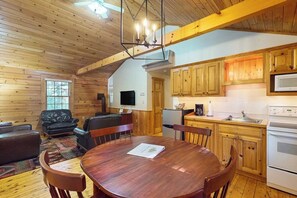 L’intérieur d’un chalet en bois comprend une table à manger, des chaises, un canapé, un téléviseur et un coin cuisine avec des meubles et des appareils électroménagers en bois.