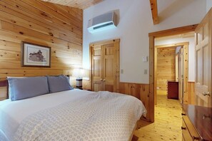Een kamer met houten lambrisering, een bed, een ingelijste foto aan de muur en een deur naar een andere kamer.