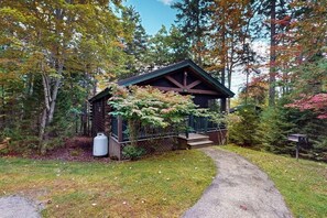 Eine Hütte mit Veranda, umgeben von Bäumen und einem Schotterweg.