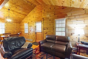 Ein Holzblockhaus-Interieur mit einem Ledersofa, einem Esstisch und einer Chandelier.