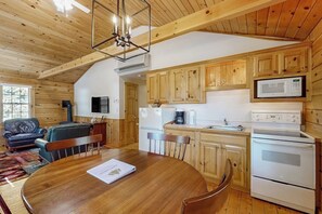 Ein Holzinterieur mit Esstisch, Stühlen, einer Couch und einer Küche mit Holzschränken, einer Mikrowelle und einem Herd.